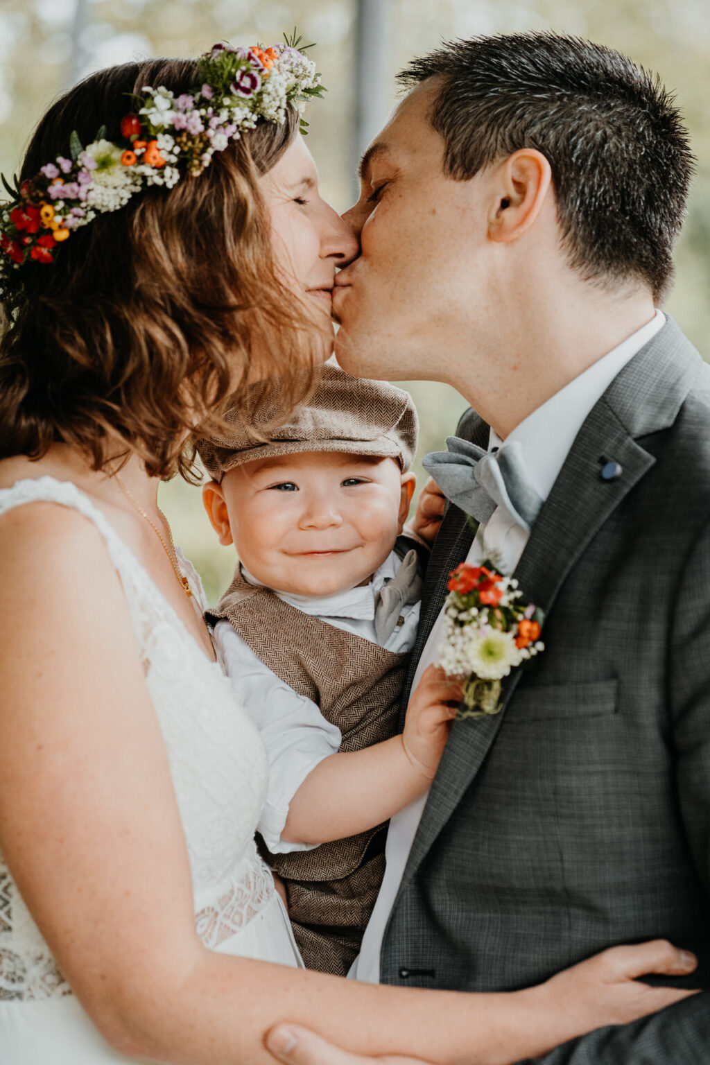 Hochzeitsfoto von küssenden Brautpaar und deren kleinen Sohn dazwischen