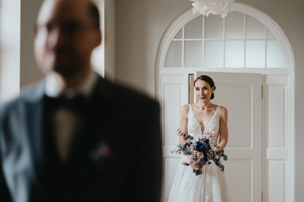 Die Braut kommt auf dem Bräutigam zu, er sieht sie noch nicht weil sie hinter ihm steht.