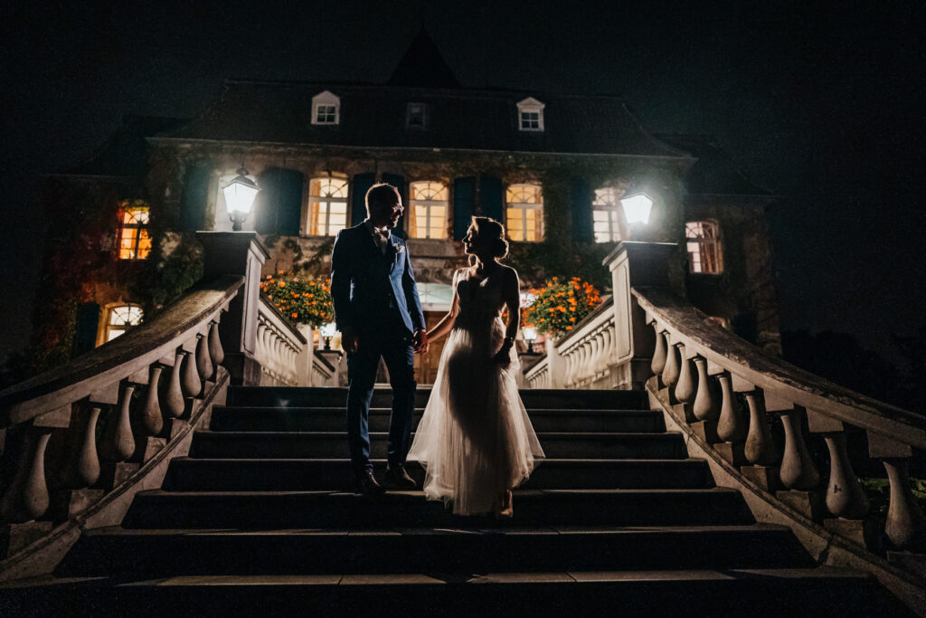 Das Brautpaar steht im dunkeln auf der Treppe vorm Schloss Linnep und wird nur von den Lampen leicht beleuchtet