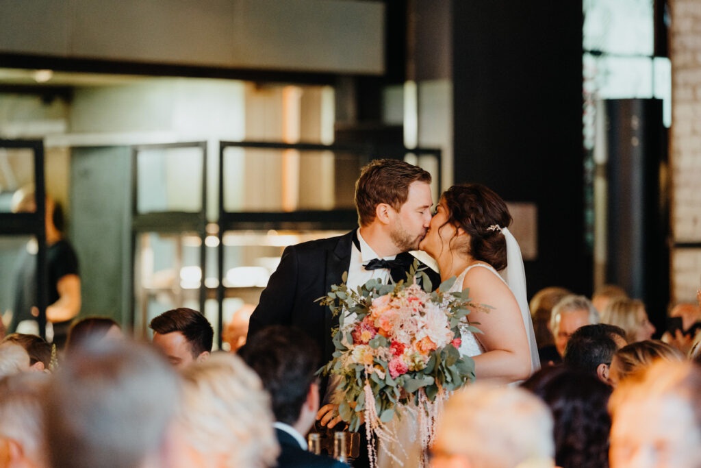 Die Braut und der Bräutigam küssen sich in der Seifenfabrik in Düsseldorf und alle Gäste applaudieren